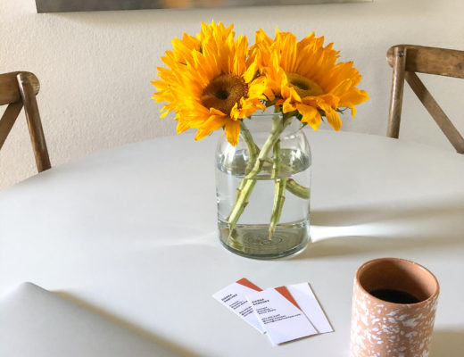 white table with sunflowers in glass vase, cup of coffee and a macbook air laptop showcasing business cards